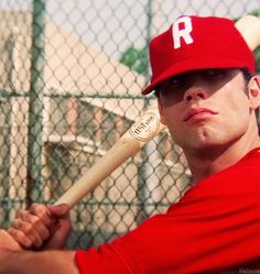 a man holding a baseball bat in front of a fence