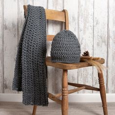 a knitted hat and scarf sitting on top of a wooden chair next to a pine cone