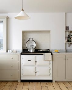 a white stove top oven sitting inside of a kitchen next to wooden floors and cabinets