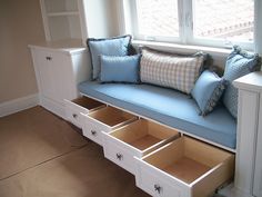 a white bench with drawers underneath it in front of a window and some windowsills