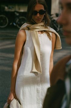 a woman walking down the street wearing sunglasses and a white dress with a scarf around her neck