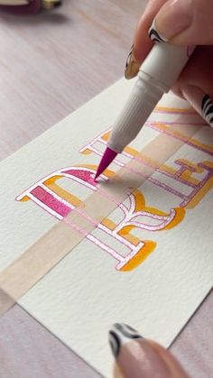 someone is using a marker to draw letters on paper with colored pencils and markers