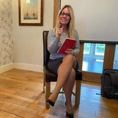 a woman sitting in a chair holding a red book and giving the thumbs up sign