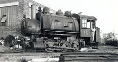 an old black and white photo of a train on the tracks in front of a brick building