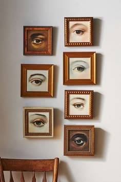 several framed pictures hang on the wall next to a wooden chair with an eyeball painted on it