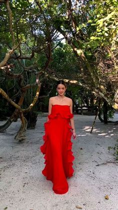 a woman in a red dress standing under some trees