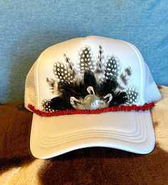 This beautiful white trucker hat with black & white colored feathers, a silver buffalo nickel concho embellishment, and a removable red stone hat band will be all anyone can talk about when you wear it.  It's such a fun way to spice up any outfit and the places to wear this hat are endless. Be prepared for loads of compliments.  The feathers are handpicked for each hat.  The hat has a foam front, mesh back, and an adjustable snap back. Western White Cap Hat, White Country Style Trucker Hat With Curved Brim, Country Style White Snapback Hat, Country Style White Baseball Cap, White Country Style Trucker Hat, Adjustable White Country Trucker Hat, Country Style White Snapback Trucker Hat, White Adjustable Country Trucker Hat, Adjustable White Country Style Trucker Hat