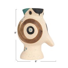 a white and brown ceramic animal head with black spots on it's face, next to a ruler