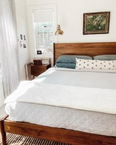 a bed with white sheets and blue pillows in a bedroom next to a painting on the wall