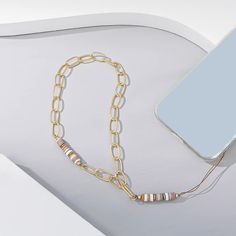 a cell phone laying on top of a table next to a gold chain and necklace