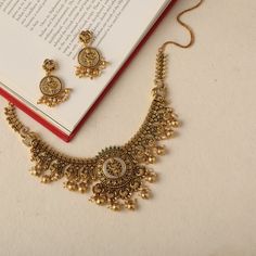 Description : Tarinika presents a necklace with a temple-inspired design, showcasing an elaborate depiction of Goddess Lakshmi, adorned with intricate florals and peacock patterns that impart a sense of grandeur. Embellished with golden drop beads, this necklace serves as a striking statement piece, perfect for inclusion in your Wedding Wishlist. Details & Specification : Materials used: Brass Alloy with Antique Gold Plating Weight - Necklace-72.30 gm, Earrings-16.90gm Length - Necklace-14cm, Ea Antique Gold Jewelry Indian Necklaces, Gold Necklace Set Indian, Traditional Gold Jewellery, Jewelry Pics, Antique Necklace Set, Antique Necklace Gold, Antique Gold Necklace, Temple Necklace, Wedding Wishlist