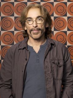 a man with glasses and a mustache standing in front of a checkerboard wall