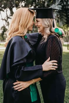 two women hugging each other in graduation gowns and caps, one wearing a green tassel