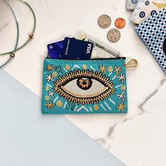 a blue purse with an eye on it next to some coins and other items that are sitting on a table