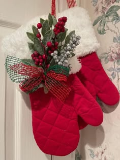 a pair of red mitts hanging from a door with holly and berries on it