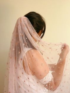 a woman wearing a wedding veil with stars on the side and her arms behind her head