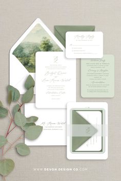 the wedding stationery is laid out on top of each other, with greenery and foliage