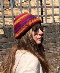 a woman wearing sunglasses and a knitted hat is standing in front of a brick wall