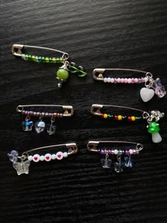 four hair clips with beads and charms on them sitting on a table together, one has a heart shaped brooch