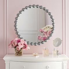 a white dresser topped with a mirror next to a vase filled with pink roses and flowers