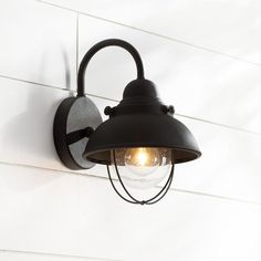 an outdoor light mounted on the side of a white wall with a black lamp shade