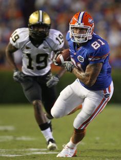 a football player running with the ball in his hand and another person behind him on the field