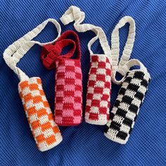 four crocheted bottles are lined up on a blue surface, one is red and the other is white