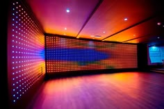 an empty room with colorful lights on the wall and wood flooring in front of it