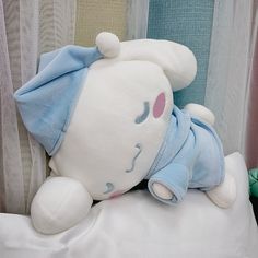 a white stuffed animal laying on top of a bed next to a blue and white curtain