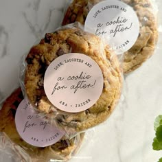 three cookies wrapped in plastic on top of a marble countertop with handwritten labels