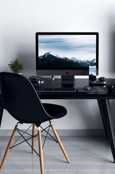 a desk with a computer monitor and keyboard on top of it next to a black chair