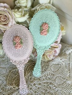 two pink and blue mirrors sitting on top of a lace covered tablecloth next to flowers