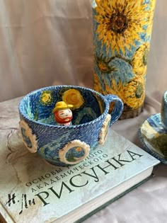 there is a cup and saucer sitting on the table next to a vase with a doll in it