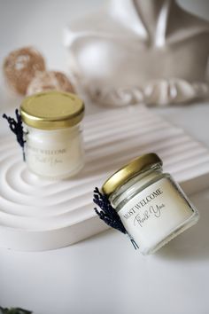 two small jars are sitting on a white tray next to some flowers and a vase