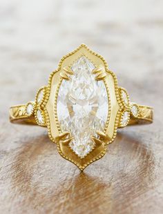 a yellow gold ring with a pear shaped diamond in the center on a wooden surface