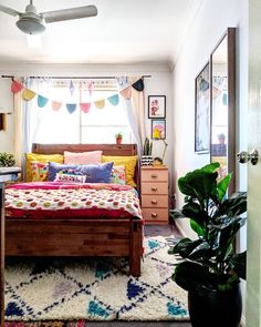 a bed room with a neatly made bed next to a window and a potted plant