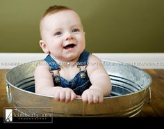 a baby sitting in a metal bucket smiling