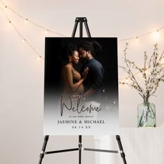 an easel with a sign that says welcome to the couple on it and lights in the background