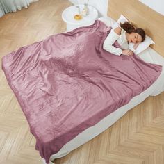 a woman laying in bed with a pink blanket on it's side and her head resting on the pillow