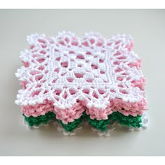 a crocheted doily with pink and white flowers on the edges, sitting on a table