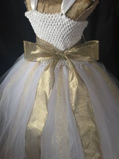 This gorgeous gown is the perfect choice for any special occasion. The white and gold dress, has an empire waist and is floor length. Gold glitter strands of tulle are added throughout the dress for extra sparkle! A large golden sash, can be tied in a variety of ways! The white crochet top is not see-through and has a super soft lining for added comfort. The wide, white satin ribbon straps, criss-cross and tie in the back for an extra secure fit. They will love to twirl in this one! While measur White Tulle Ball Gown For Dress-up, Gold Tulle Prom Gown, Gold Tulle Gown For Prom, Princess Style Gold Gown For Dress-up, Gold Princess Pageant Dress For Dress-up, Elegant Gold Tulle Gown, Elegant Gold Tulle Ball Gown, White Princess Ball Gown For Prom, White Ball Gown Princess Dress For Prom