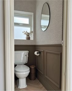 a white toilet sitting next to a window in a bathroom under a large round mirror