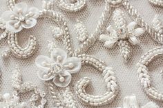 the fabric is white and has flowers on it with pearls, beads and sequins