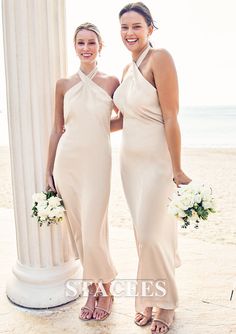 two women standing next to each other in front of a white column on the beach