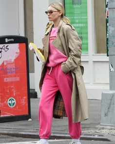 a woman in pink pants and trench coat crossing the street with her hand on her hip