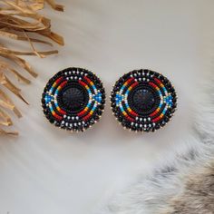 These earrings are made with seed beads and black centers encircled in black rhinestone. They are then branded with our logo, backed with moose hide and your choice of earring findings. The edging is done with black rondelle beads, creating and extra bit of sparkle as the earrings move about. Each pair are made with hypoallergenic materials for sensitive ears. Don't see a  color palette you like? Send me a message with your ideal color palette and I will do my best to bring your idea to life! Circle Beaded Earrings, Indigenous Beaded Earrings, Round Beaded Earrings, Native American Beadwork Earrings, Black Beaded Earrings, Seed Beaded Earrings, Antler Earrings, Beautiful Beaded Earring, Native American Beadwork Patterns