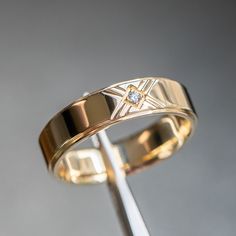 a gold wedding band with a diamond in the center on a metal stand against a gray background