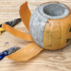 a pumpkin shaped container sitting on top of a wooden table next to pliers and scissors