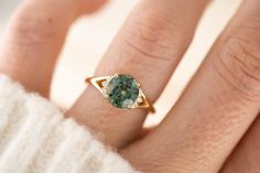 a close up of a person's hand wearing a ring with a green stone