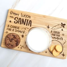 a wooden cutting board with cookies and milk on it that says from lucia to santa